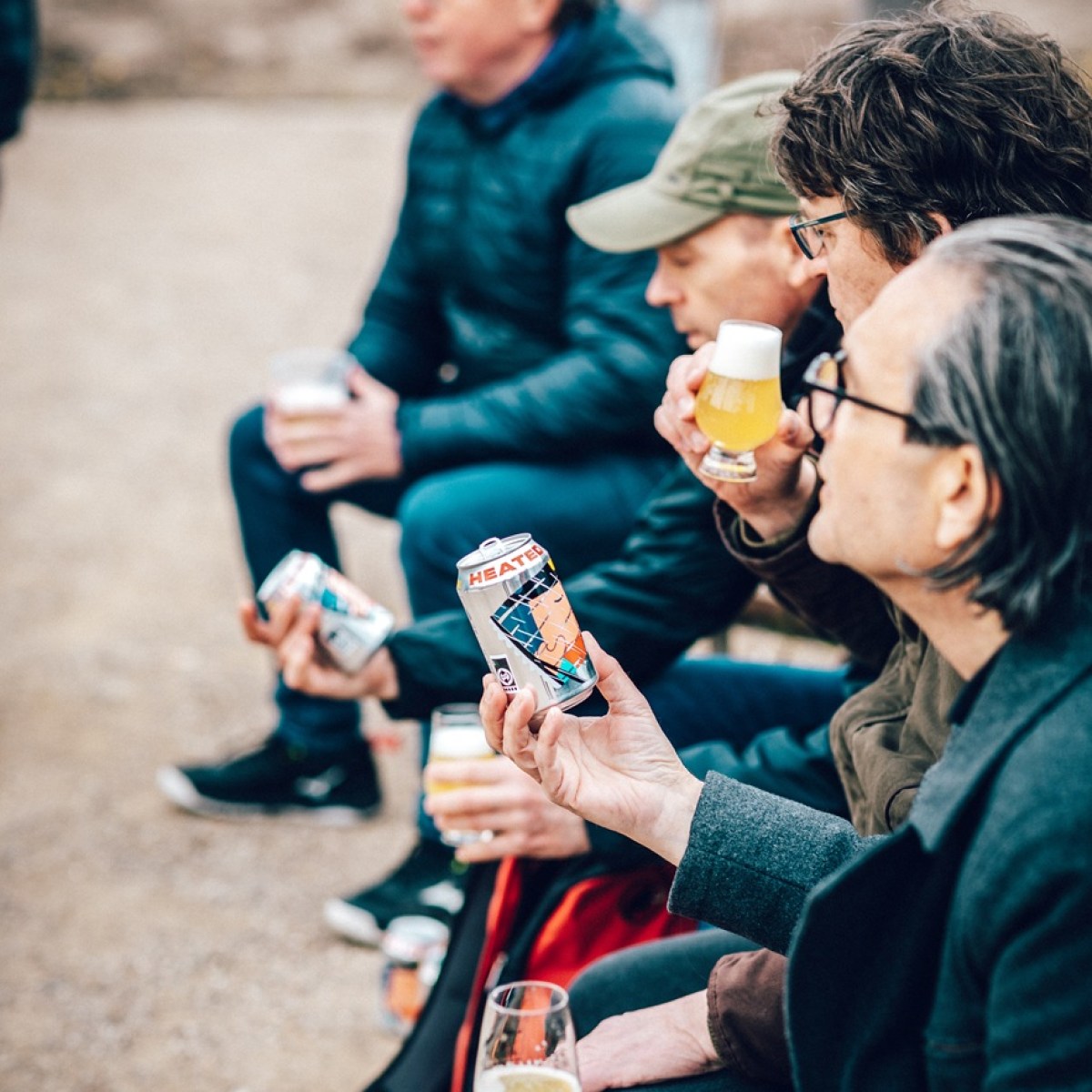 Four people sitting outdoors, holding and examining cans of beer.