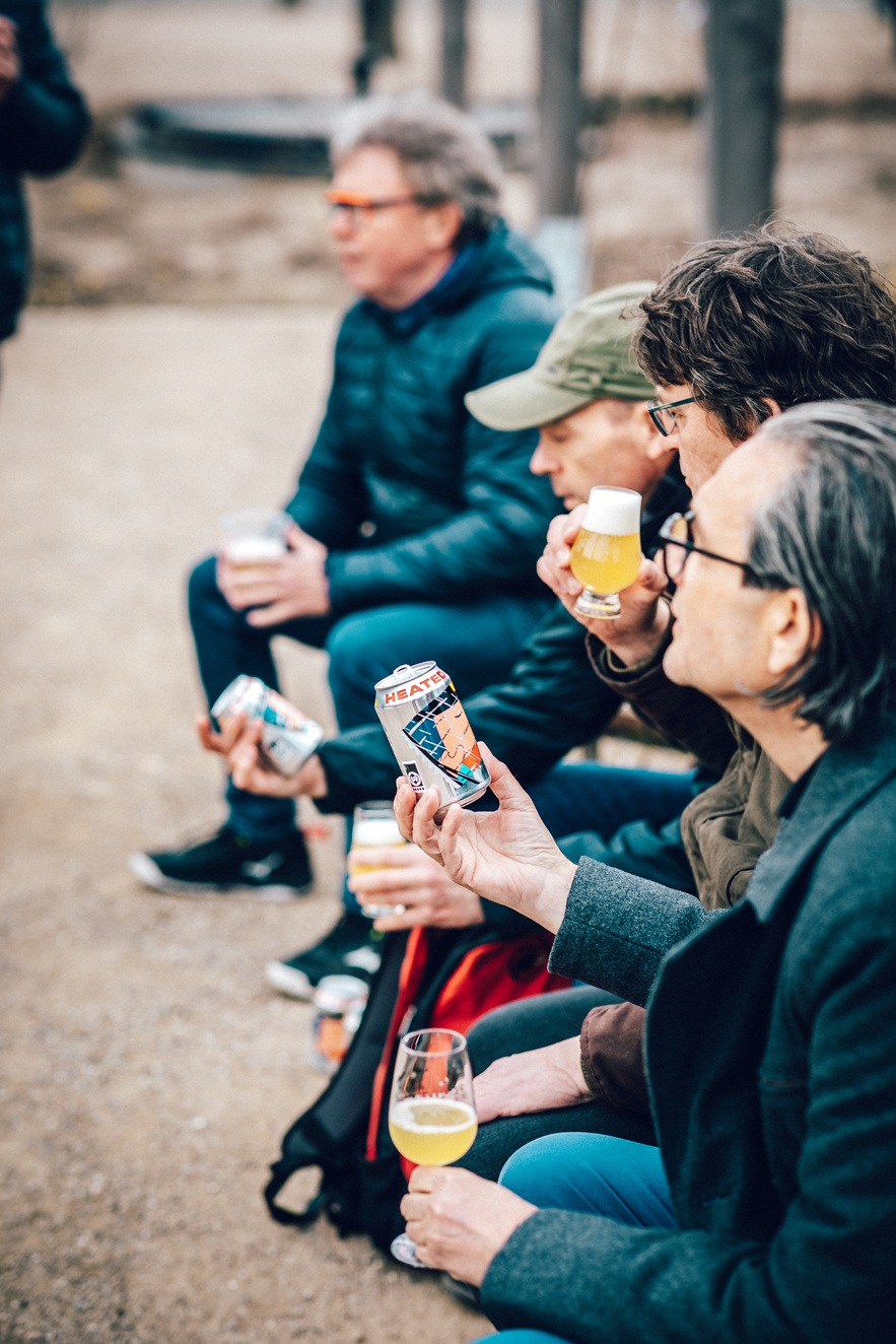 Four people sitting outdoors, holding and examining cans of beer.
