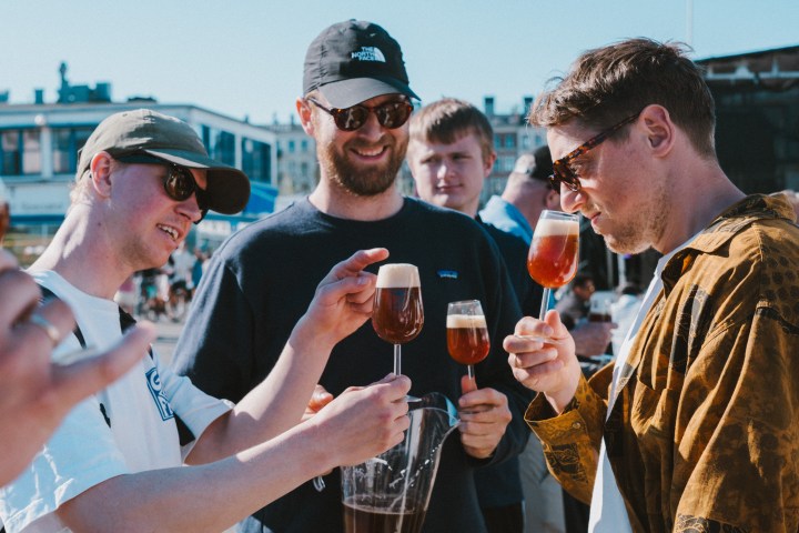 Four men outdoors smiling and holding beer glasses.