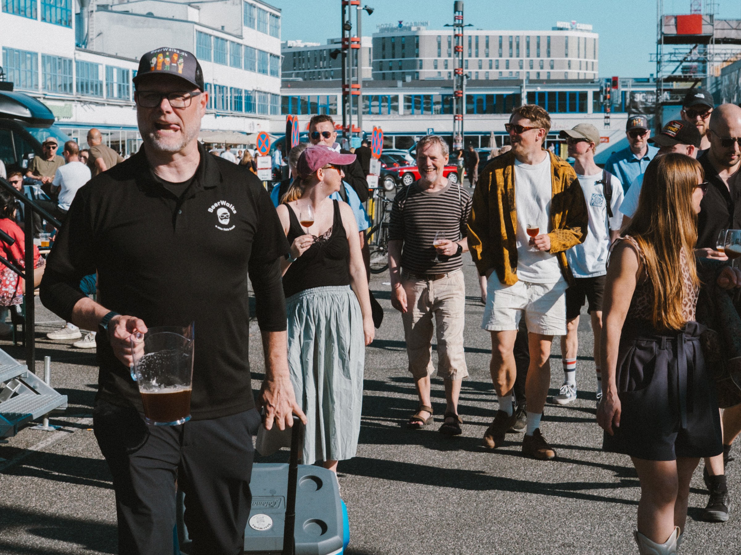 People walking outdoors, man in black with drink, urban background.