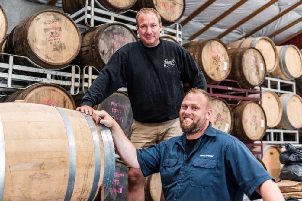 Two people in a barrel storage room, smiling and standing near wooden barrels.